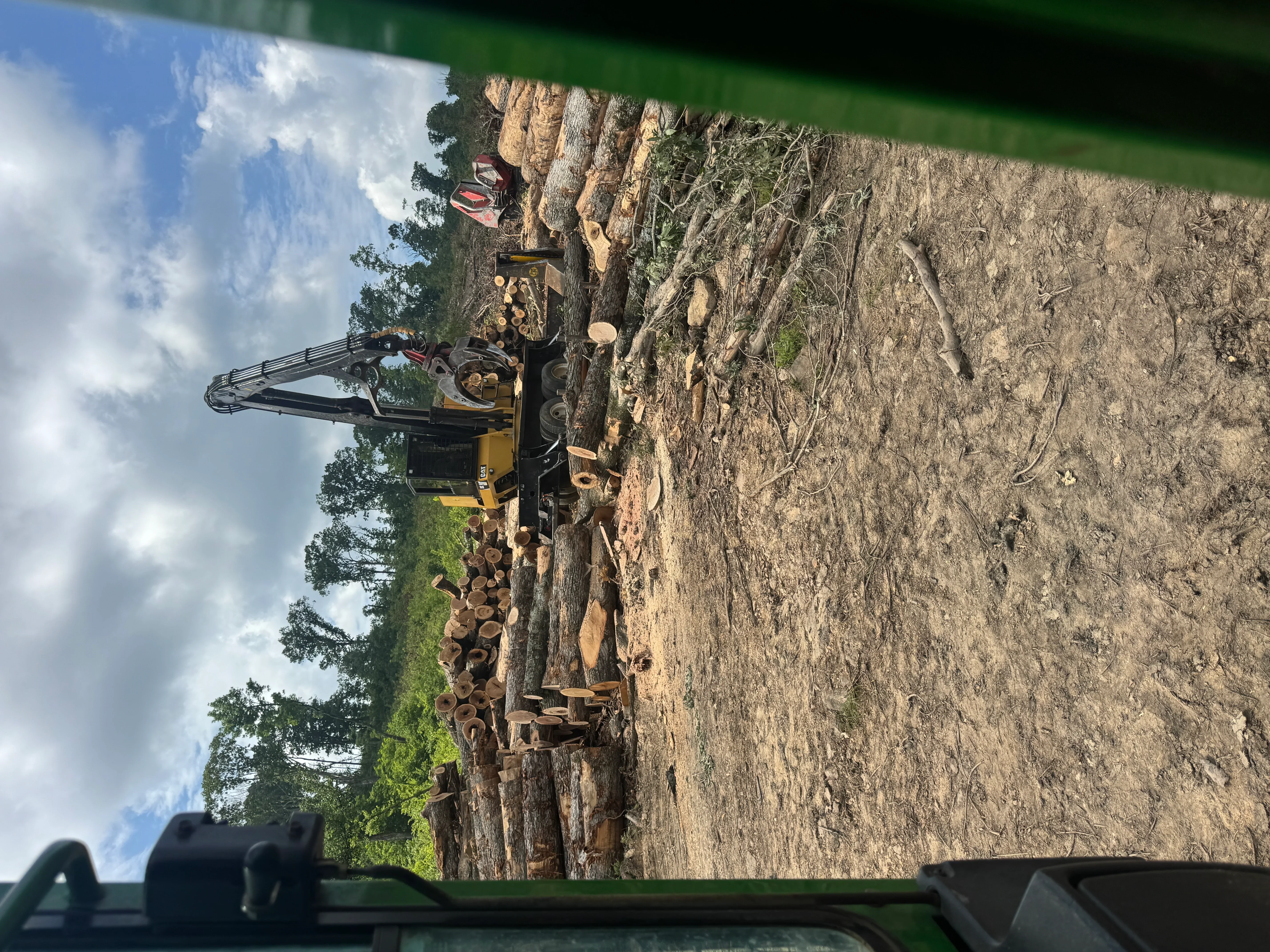 Tracked excavator with hydraulic grapple processing felled logs on cleared timber site