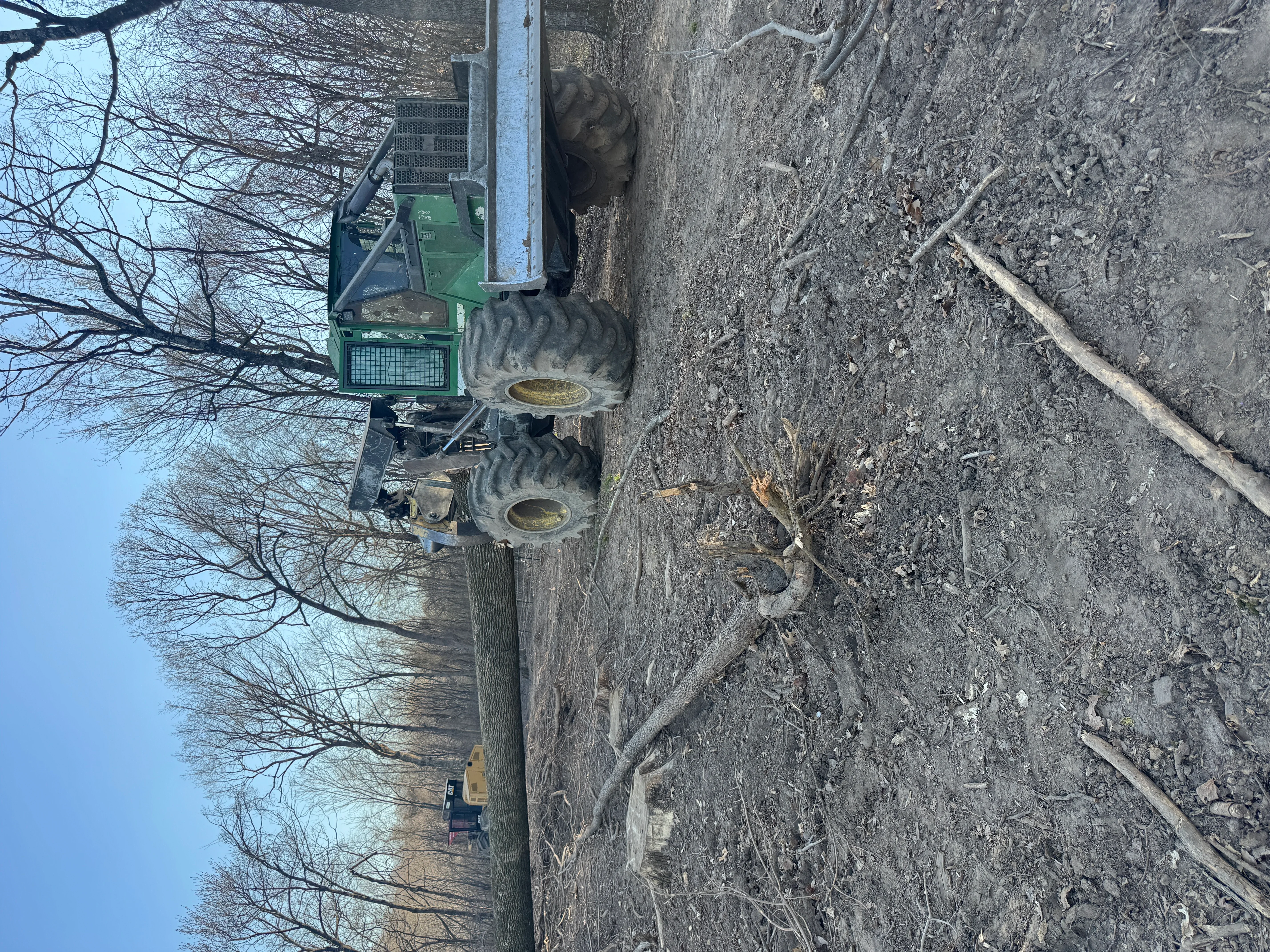 Green tracked skidder with grapple removing brush and debris from cleared land